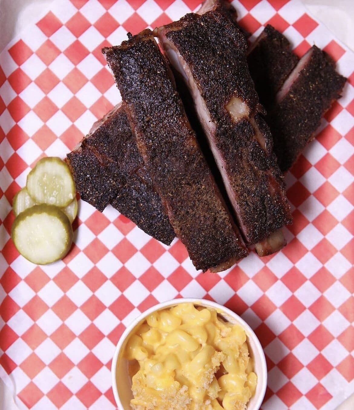 Smoked ribs and pickle chips on a red-and-white checkered tablecloth